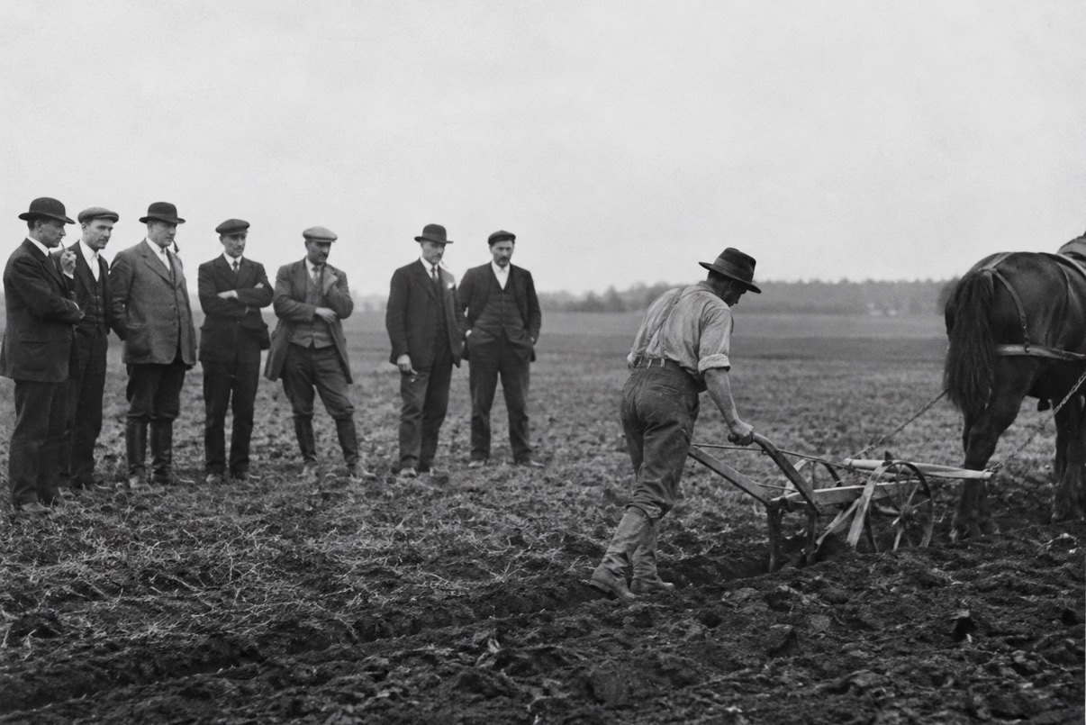Archival photograph: men watching the first plough turn a field