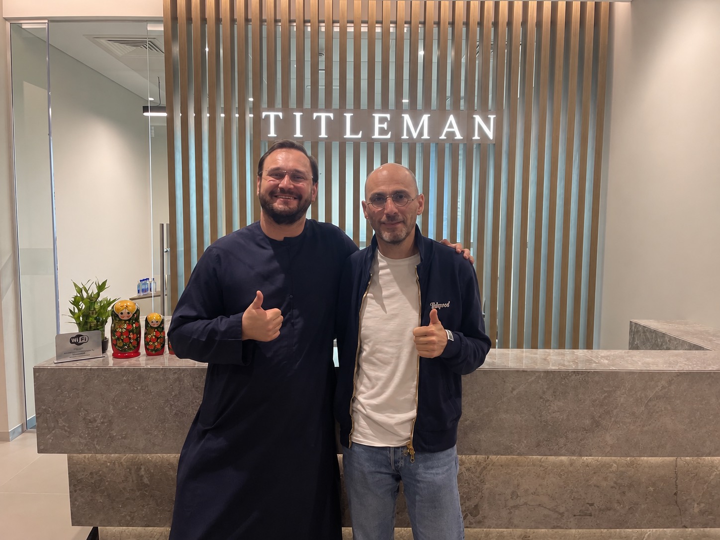 Two colleagues at the office reception desk under the lit TITLEMAN sign