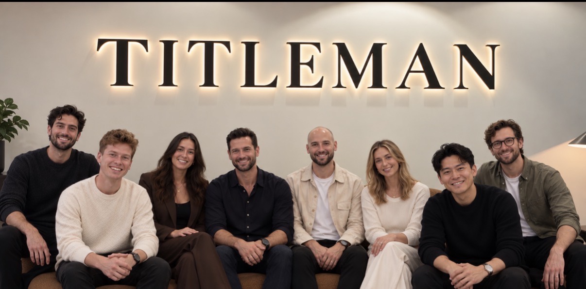 Eight of the team on a sofa beneath the backlit TITLEMAN wordmark in the office