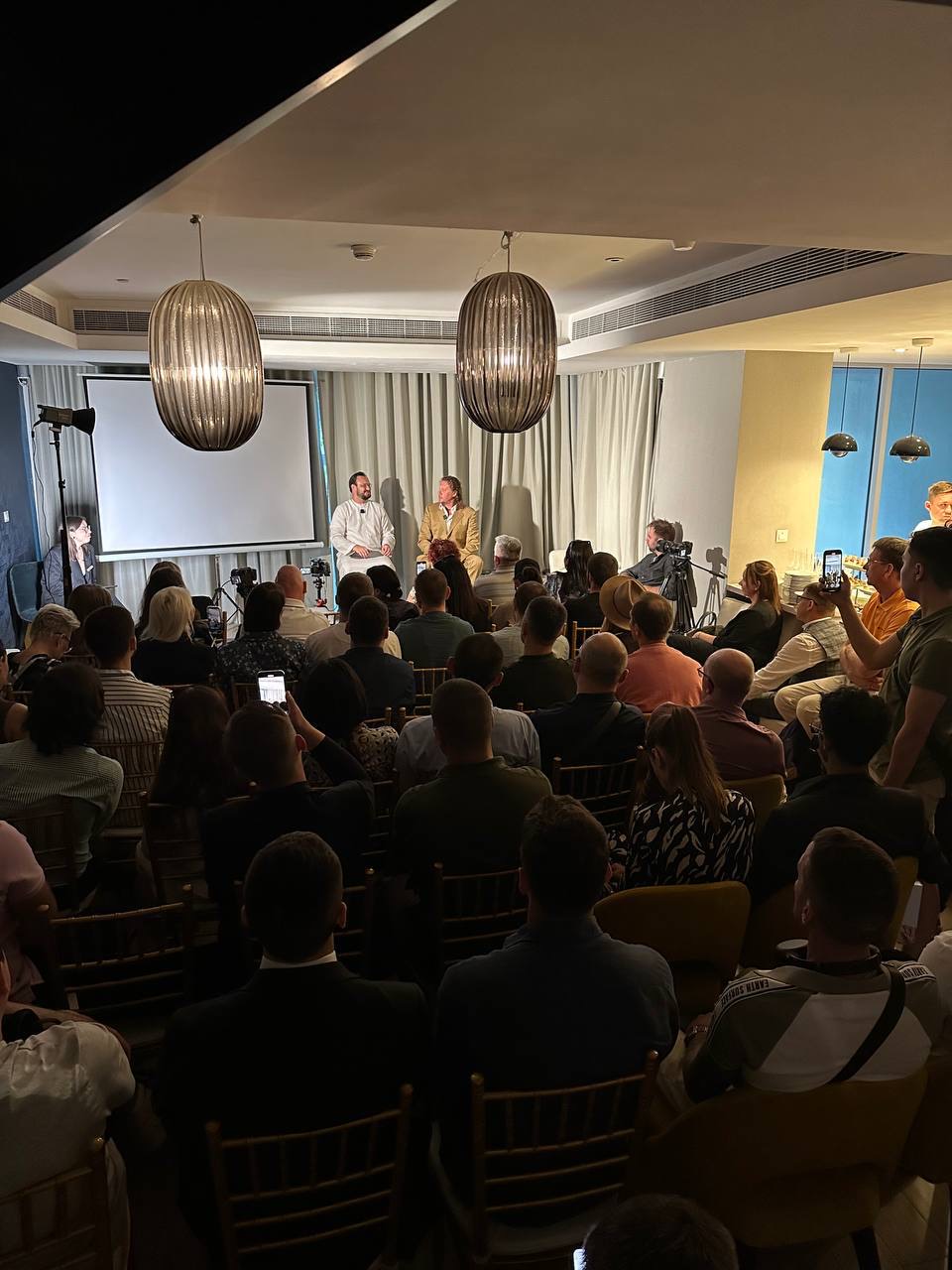 An evening panel in front of a full room, cameras at the back