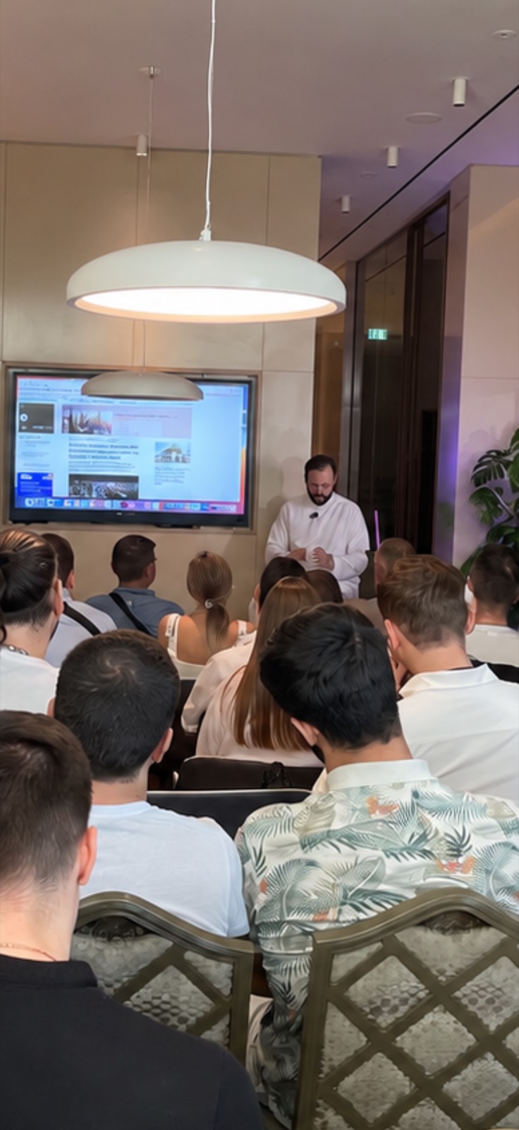 A seminar in a hotel lounge, the room seated and a property page up on the screen